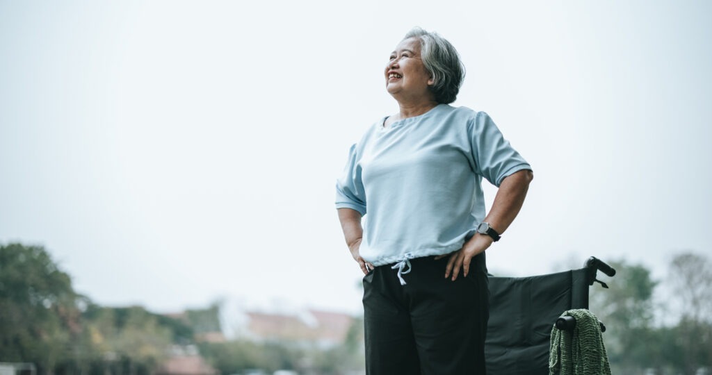 mature asian woman standing in front of wheelchair smiling