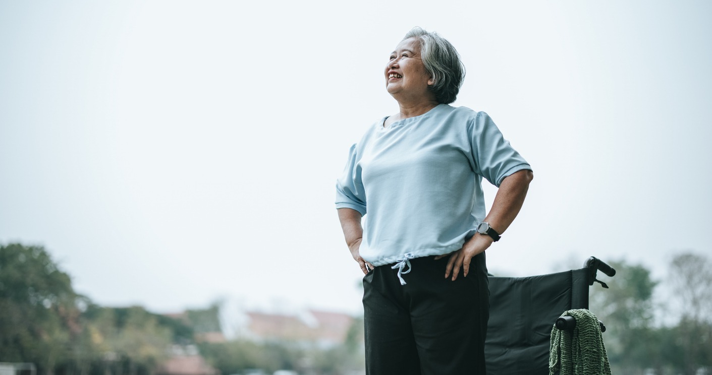 mature asian woman standing in front of wheelchair smiling