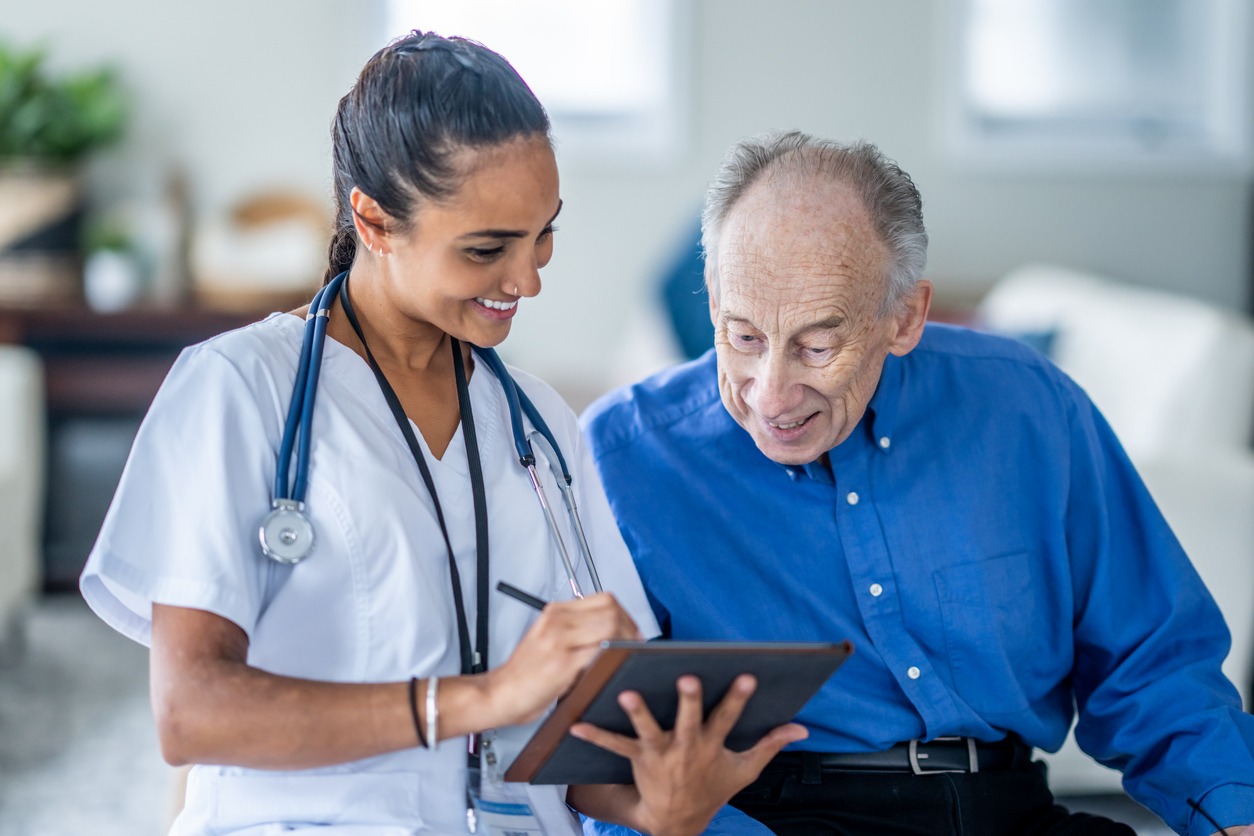 senior man talking with female health worker while they both look at a tablet