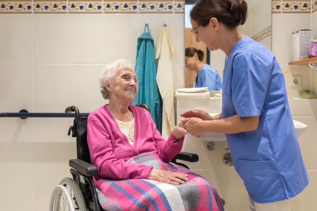 senior woman in wheelchair being helped by healthcare worker in a bathroom senior woman in wheelchair being helped by healthcare worker in a bathroom
