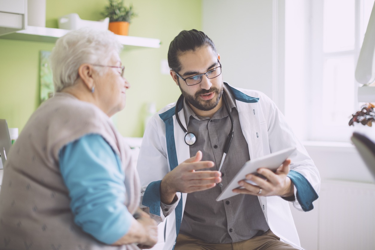 senior woman reviewing a tablet with a doctor in exam room senior woman reviewing a tablet with a doctor in exam room