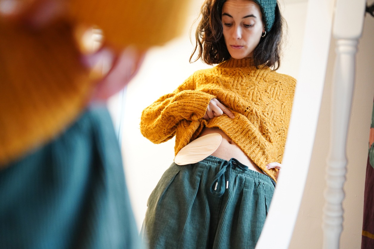 reflection of a woman looking at the ostomy bag in the mirror at home